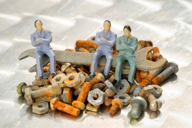 üretim toplantı kavramı. Üç işadamı minyatür insanlar oyuncak sittiong bir İngiliz anahtarı ve yığın eski paslı ve vidalar