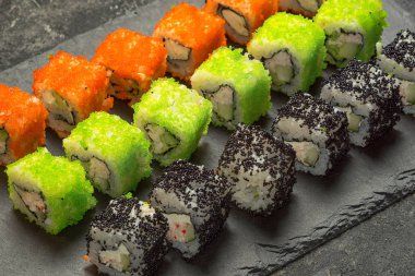 Siyah taş tabağa çeşitli Japon suşi yemek ayarla, görüş açısı kadar yakın. Ton balığı, somon, karides, yengeç ve avokado ile rulo. Sushi menüsü.