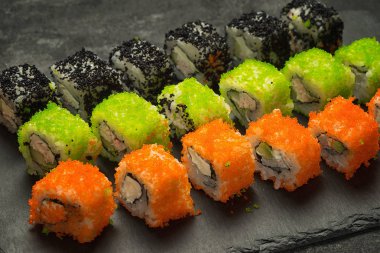 Siyah taş tabağa çeşitli Japon suşi yemek ayarla, görüş açısı kadar yakın. Ton balığı, somon, karides, yengeç ve avokado ile rulo. Sushi menüsü.