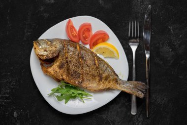 Siyah masada beyaz çanak üzerinde ızgara dorado balık. Üstte görüntü.