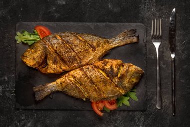 Siyah masa üzerinde koyu siyah granit taş tahta üzerinde iki ızgara dorado balık. Üstte görüntü.