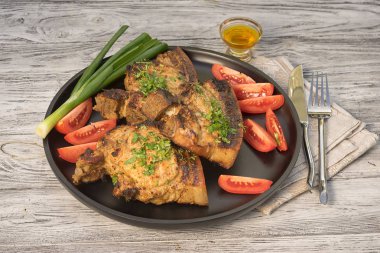 Domates ve yeşil soğan ile siyah ahşap tepsi üzerinde ızgara domuz kaburga, rustik ahşap masa üzerinde servis, üst görünümü.