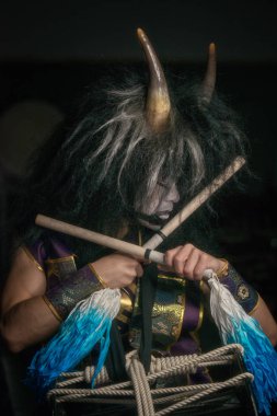 Boynuzlu ve bagetli peruklu bir iblisin profil portresini kapat. Japon Taiko davulcusu.