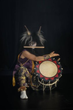 Boynuzlu ve şeytani maskeli bir peruklu Taiko davulcusu sahnede otururken siyah bir arka planda davul çalıyordu. Japon mitolojisindeki şeytan..