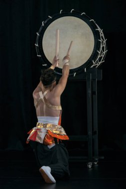 Taiko drummer hits the big drum on stage on a black background, back view. clipart