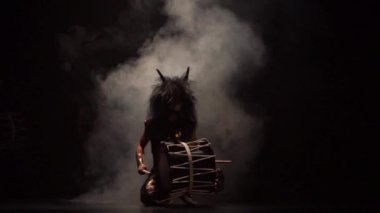 Sahnede dört sanatçı peruklu ve makyaj davulu Taiko 'yu dumanlı karanlık bir arka plana itiyor. Japon mitolojisindeki şeytanlar.
