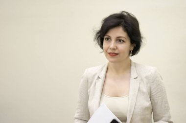 Başarılı bir özgüven portresi. Elinde fotokopi odası olan gülümseyen bir iş kadını. Çekici orta yaşlı kadın, iş elbisesi içinde güzel bir gülümsemeyle beton bej duvara karşı..