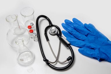 Stetoskop, mavi eldivenler, şırıngalar, şişeler, şişeler beyaz bir masanın üzerine yerleştirilmiş.