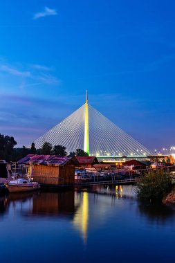 Belgrad, Sırbistan - 20 Haziran 2018: Sava nehri üzerindeki Belgrad yat limanının yansımasıyla gece Ada köprüsünün yan görünümü