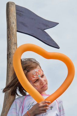 Güzel bir kız bir yüz boyama ve şekil kalp bir balon tutan vardır