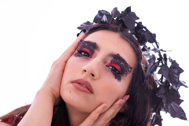 Çekici Genç Kadın Model Portresi. Kız beyaz bir arka plan ile bir stüdyoda başında süslemeleri ile poz veriyor. Dekorasyon gibi siyah ve kırmızı yapraklar. Gözlerde fantastik makyaj.