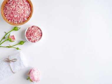 Spa yassı kompozisyonu. Tahta kavanozda deniz tuzu, havlu, beyaz arka planda çiçek. Üst Manzara. Günlük bakım konsepti, rahatlama ve dinlenme, banyo prosedürü.