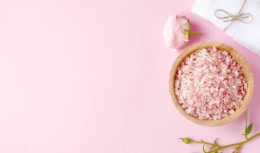 Spa yassı kompozisyonu. Ahşap kavanozda deniz tuzu, havlu, pembe arka planda çiçek. Üst görünüm, telif alanı, afiş. Günlük bakım konsepti, rahatlama ve dinlenme, banyo prosedürü.