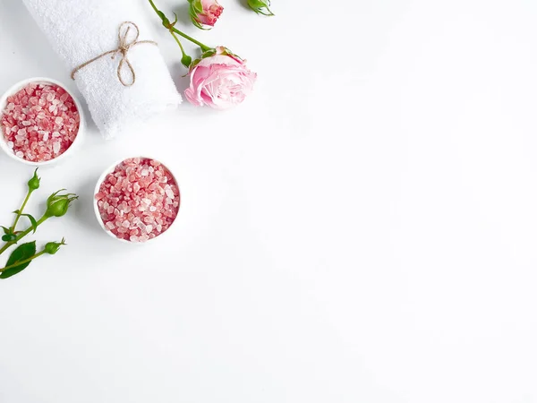 Spa yassı kompozisyonu. Kavanozda deniz tuzu, havlu, beyaz arka planda çiçek. Üst Manzara. Günlük bakım konsepti, rahatlama ve dinlenme, banyo prosedürü.