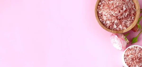Spa yassı kompozisyonu. Kavanozda deniz tuzu, pembe arka planda çiçek. Üst görünüm, telif alanı, afiş. Günlük bakım konsepti, rahatlama ve dinlenme, banyo prosedürü.