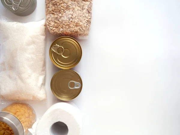 Kuru yiyecekler, stoklar, ev konsepti için gıda malzemeleri. Konserveler, makarna, yulaf ezmesi, şeker, beyaz arka plan üzerine tuvalet kağıdı, telif alanı, düz yatak