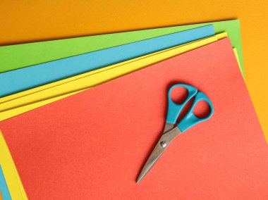 Mavi makas turuncu arka planda renkli kağıtlar üzerinde. El sanatları, el yapımı origami, dekoratif