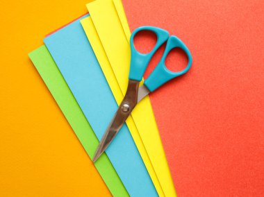 Mavi makas turuncu arka planda renkli kağıtlar üzerinde. El sanatları, el yapımı origami, dekoratif
