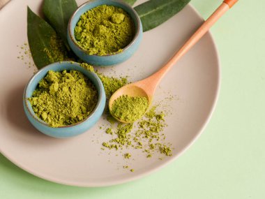 Gri tabakta kibrit çayı, büyük arka planda kaşık ve yaprak. Sağlıklı içeceği hesaba kat, kapat.