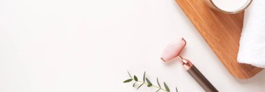 Yüz masajı yeşim taşıyla havlu, beyaz arka planda küçük bir bitki. Konsept cilt bakımı ve güzellik rutini, düz döşeme, döşeme, telif alanı.