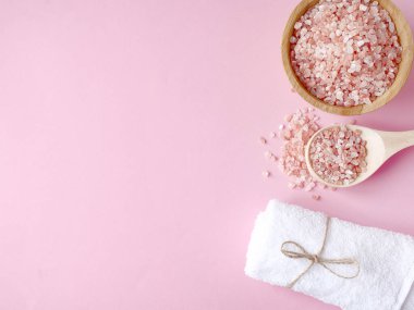 Spa yassı kompozisyonu. Tahta kavanozda deniz tuzu ve kaşıktan yayılmış pembe arka planda havlu. Kopyalama alanı, üst görünüm. Evde bakım konsepti, rahatlama ve dinlenme, banyo prosedürü.