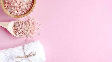 Spa yassı kompozisyonu. Tahta kavanozda deniz tuzu ve kaşıktan yayılmış pembe arka planda havlu. Kopyalama alanı, afiş, üst görünüm. Evde bakım konsepti, rahatlama ve dinlenme, banyo prosedürü.