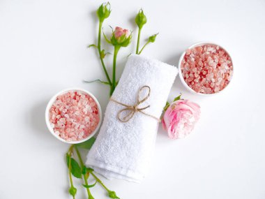 Spa yassı kompozisyonu. Tahta kavanozda deniz tuzu, havlu, beyaz arka planda çiçek. Üst Manzara. Günlük bakım konsepti, rahatlama ve dinlenme, banyo prosedürü.