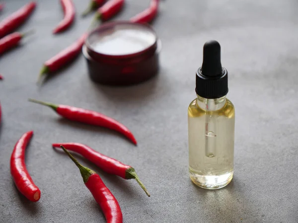 Gri arka planda kırmızı biberli organik yağ. Sakal bakımı, cilt bakımı ve saç bakımı için doğal insan kozmetiği kavramı.