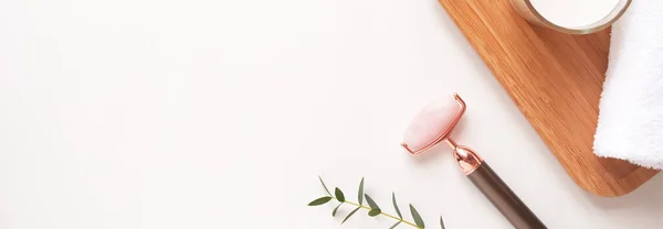 Yüz masajı yeşim taşıyla havlu, beyaz arka planda küçük bir bitki. Konsept cilt bakımı ve güzellik rutini, düz döşeme, döşeme, telif alanı.