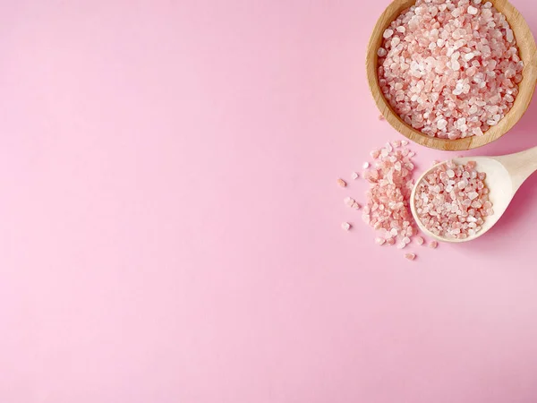 Spa yassı kompozisyonu. Tahta kavanozda deniz tuzu ve kaşıktan saçılmış, pembe arka planda banyo havlusu. Kopyalama alanı, üst görünüm. Evde bakım konsepti, rahatlama ve dinlenme, banyo prosedürü.