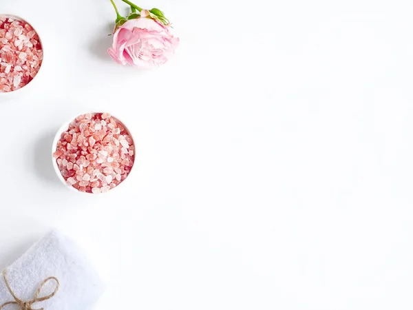 Spa yassı kompozisyonu. Kavanozda deniz tuzu, havlu, beyaz arka planda çiçek. Üst Manzara. Günlük bakım konsepti, rahatlama ve dinlenme, banyo prosedürü.