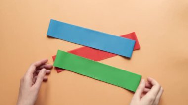 Kadın renkli fitness lastiğini esnetiyor ve turuncu arka planda farklı gerilim gösteriyor. Kavram eğitimi, spor, kilo verme, egzersiz, sağlıklı yaşam tarzı, genişleticiler, üst görünüm.