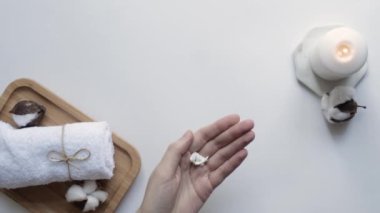 Genç kadınlar siyah kavanozdan beyaz arka plana krem sürerler. Spa, rahatlama, bakım, nemlendirici, güzellik küresi, kişisel bakım atmosferi. Üst görünüm.
