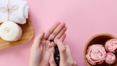 Genç kadınlar pembe arka planda siyah kavanozdan elde krem sürerler. Spa, rahatlama, bakım, nemlendirici, güzellik küresi, kişisel bakım atmosferi. Üst görünüm
