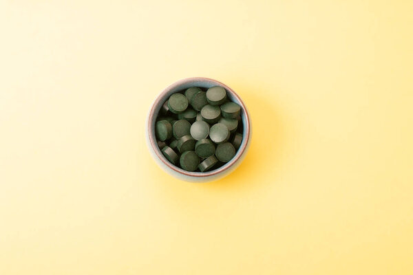 спирулина в таблетках в банке на желтом фоне. Концепция натуральная, эко, порошок здоровой пищевой добавки.