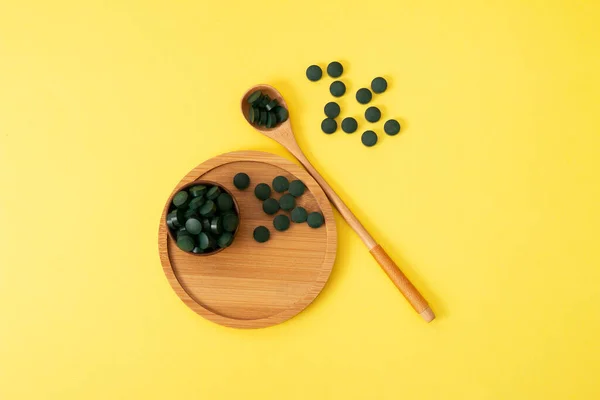 Sarı arka planda tahta kaşık ve kavanozla tabletlerde spirulina. Doğal, eko, toz sağlıklı beslenme takviyesi.