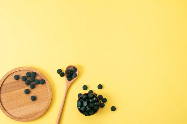 Sarı arka planda tahta kaşık ve kavanozla tabletlerde spirulina. Doğal, eko, toz sağlıklı beslenme takviyesi kavramı. Kopyalama alanı
