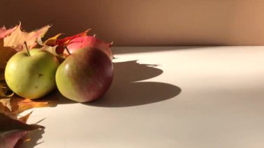Akçaağaç yapraklı birkaç elma kahverengi arka plandaki masada sert ışıkla yatıyor. Sonbahar atmosferi, konforlu zaman, hasat, metin için alan, video pankartı.