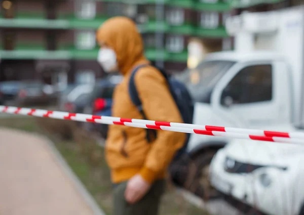 Kapüşonlu ve koruyucu maskeli bulanık bir adam sokakta çitlerin arkasında. Evde kal. Coronavirüs veya covid 19 karantina.