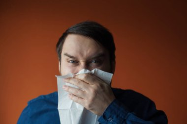 Siyah saçlı, mavi gözlü, hapşıran ve önünde mendil tutan beyaz bir adam. Hasta hissediyorum, grip, virüs, gıda alerjisi.