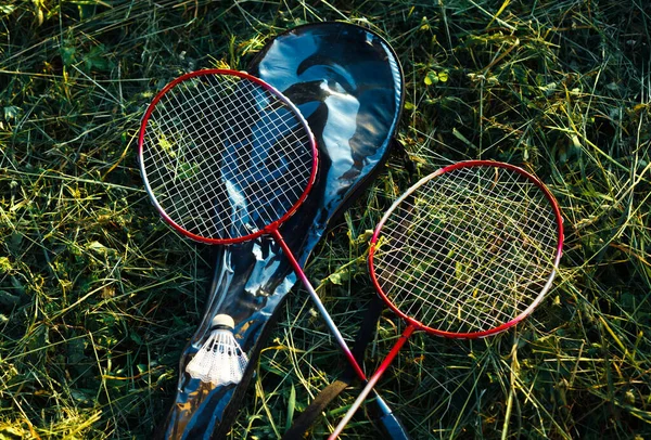 Çimlerin üzerinde yatan iki çapraz badminton raketi. Spor ve yaz açık hava aktiviteleri