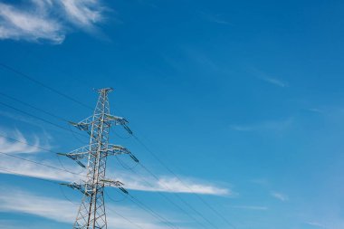 Beyaz bulutlu parlak mavi gökyüzüne karşı yüksek voltaj kulesi. Kopya alanı olan elektrik iletim hattı