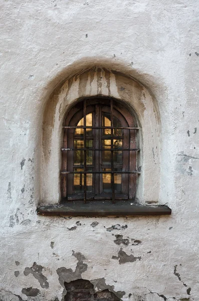 Beyazlatılmış manastır duvarındaki küçük kafeslenmiş eski pencere, ortaçağ manastırı.