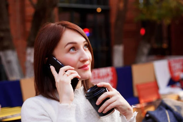 Kahvesini içerken akıllı telefonuyla konuşan gülümseyen esmer kadın. Müjdemi isterim. Çevrimiçi randevu kavramı