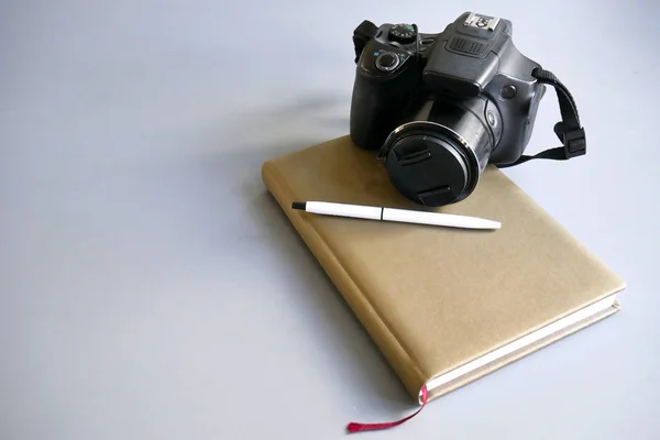 a camera with a notepad and a gray-backed pen