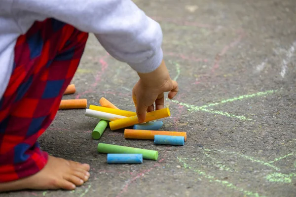 Child on the outdoor park floor, drawing doodles with chalk happy