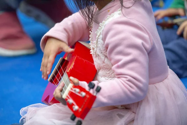 A group of children in an outdoor park, learning to play a guitar, playing with Ukulele