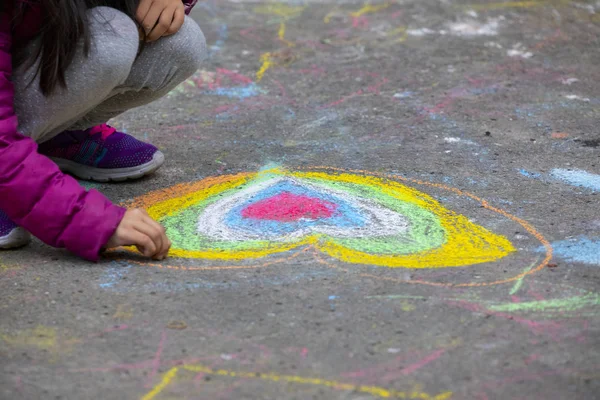 Child on the outdoor park floor, drawing doodles with chalk happy