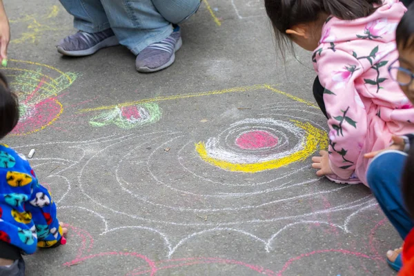 Child on the outdoor park floor, drawing doodles with chalk happy