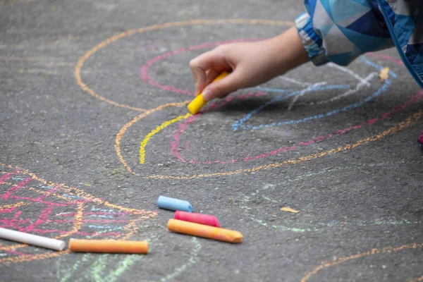 Child on the outdoor park floor, drawing doodles with chalk happy